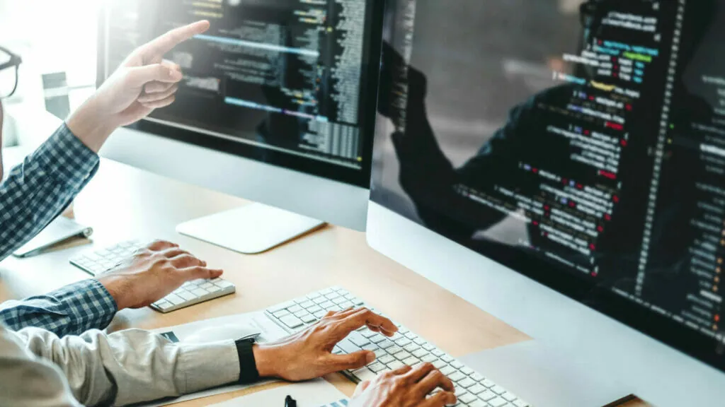 Zwei IT-Sachverständige prüfen Programmcode auf zwei Bildschirmen im Büro